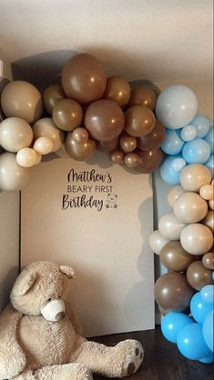 a teddy bear sitting in front of a balloon arch