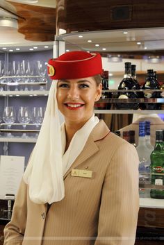 a woman wearing a red hat standing in front of shelves with wine glasses and bottles