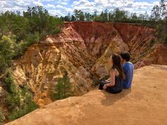 two people sitting on the edge of a cliff