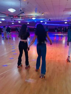 two girls on roller skates in a large room with wooden floors and blue lights