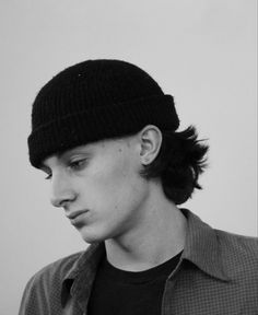 a young man wearing a beanie looking at his cell phone while standing in front of a white wall