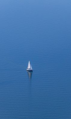 a lone sailboat floating in the blue water