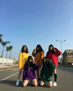 four girls are posing in the middle of an empty street with palm trees behind them