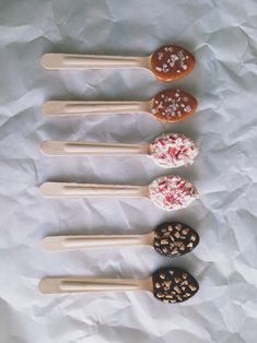 five different kinds of donuts on wooden spoons with sprinkles and chocolate