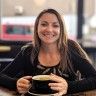 a woman sitting at a table with a plate of food in front of her smiling