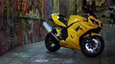 a yellow motorcycle parked in front of a graffiti covered wall