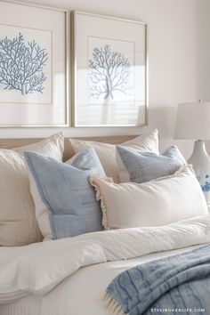 two framed pictures hang above a bed with white linens and blue pillows on it