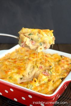 a spoon full of macaroni and cheese being lifted from a red casserole dish