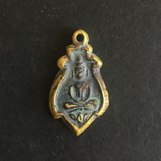 an old bronze pendant with a buddha figure on it's side, sitting on a black surface