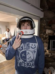 a young man wearing a helmet making the peace sign with his fingers while standing in front of a fireplace