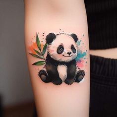 a small panda bear tattoo on the right inner arm and lower arm with watercolor paint splatters