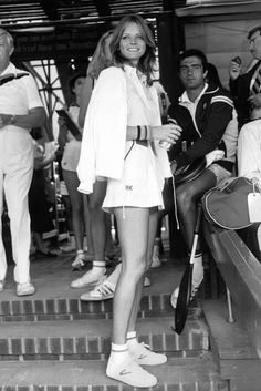 a black and white photo of a woman in tennis attire standing on steps with other people