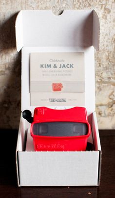 a red toy car in a white box on a wooden table next to a wall