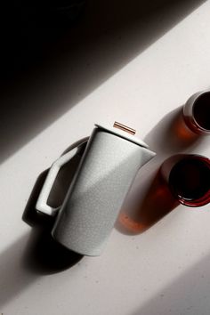 two cups sitting next to each other on top of a white counter with sunlight coming through the window