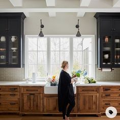 a woman standing in front of a kitchen sink with lots of counter space and cabinets