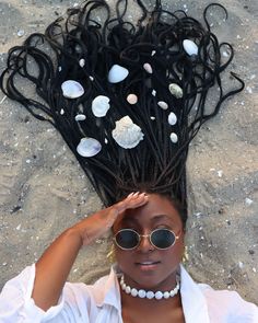 a woman laying on the beach with her hair in braids and pearls around her head