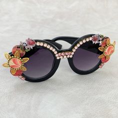 Another fabulously unique pair of embellished sunglasses from the Lenora Dame Sunnies collection! Make a statement in these round shiny black sunglass frames with black lenses. Inspired by Iris Apfel and her signature round black frames, these full of bling sunglasses are embellished with a mix of design elements. Wooden discs decoupaged in mid-century textile prints, floral metal components and Swarovski rhinestones that bring the bling making these a truly unique pair of festival sunglasses! V Black Round Frame Party Sunglasses, Party Sunglasses With Round Glass Frame, Party Round Frame Glass Sunglasses, Party Sunglasses With Gradient Round Frame, Party Sunglasses With Gradient Round Lenses, Party Sunglasses With Tinted Round Lenses, Round Tinted Lens Sunglasses For Parties, Round Tinted Sunglasses For Party, Round Tinted Sunglasses For Parties