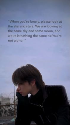 a young man sitting on top of a wooden bench next to a wall with a poem written in it