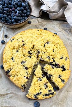 a blueberry crumb cake with one slice cut out and two bowls of blueberries in the background