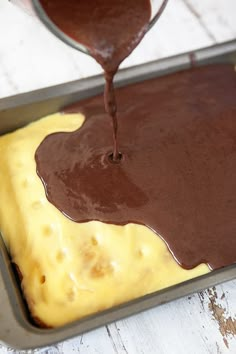 chocolate sauce being poured on top of a cake in a baking pan with yellow and brown icing