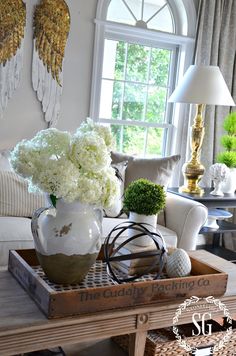 a living room filled with furniture and flowers on top of a wooden tray in front of a window