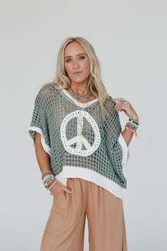 Cozy, cute, and embodying the perfect boho feel, the Peace Oasis Top brings all the peaceful vibes when you wear it! Comfy and cozy open knit fabric throughout Loose and slouchy silhouette for a relaxed fit Classic v-neckline and loose short sleeves for a comfortable, effortless look Contrast knit peace sign patchwork center design Slight high low bottom edge with ribbed knit trim along the bottom hem, sleeves, and neckline Pair with: Eye Of The Sun Padded Bralette, Frenchie Raw Edge Shorts and Bohemian V-neck Summer Sweater, Fall Beach Open Knit Top, Bohemian Knitted V-neck Top, Bohemian V-neck Knitted Top, Fall Beach Knit Top With Pointelle Knit, Casual V-neck Beach Poncho, Beach Sweater With Open Knit, Cozy Open Knit Beach Sweater, Green Knitted Beach Sweater