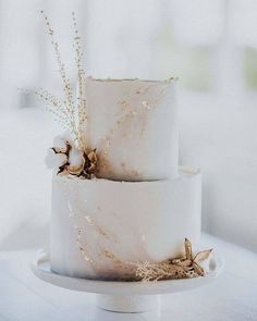 two tiered wedding cake decorated with dried flowers and gold leaf accents on a white table cloth