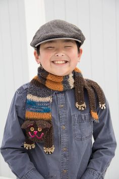 a young boy wearing a hat and scarf with his hands in his pockets, smiling at the camera