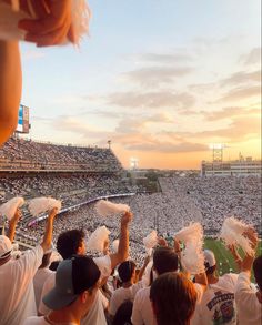 fans at a baseball game are holding their hands up in the air as the sun sets