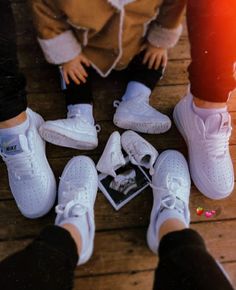 four pairs of white shoes sitting next to each other on a wooden floor in front of a person's legs