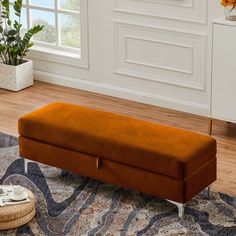 an orange bench sitting on top of a rug in a living room next to a potted plant