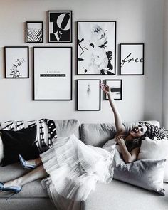 a woman laying on top of a gray couch in front of framed pictures above her