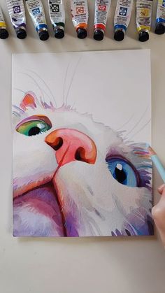 a painting of a white cat with blue eyes and pink nose, surrounded by paintbrushes