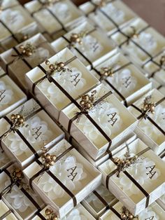 many small white boxes with brown bows and monogrammed letters on them are stacked together