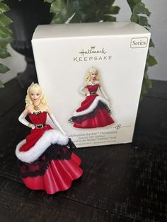 a barbie doll in a red and black dress next to a box