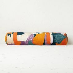 an orange and green pillow sitting on top of a white table next to a wall