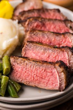 a white plate topped with meat and green beans next to mashed potatoes on a wooden table