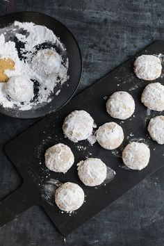 powdered sugar cookies on a baking tray next to a bowl of powdered sugar