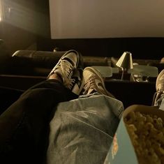 two people sitting on a couch with their feet up in front of a box of popcorn