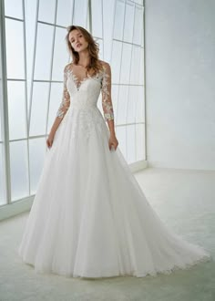 a woman in a white wedding dress standing next to a window and posing for the camera