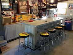 a bar with four stools and several beer bottles on the wall behind it in a garage