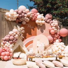 a table topped with lots of balloons next to a wooden fence covered in pink and white decorations