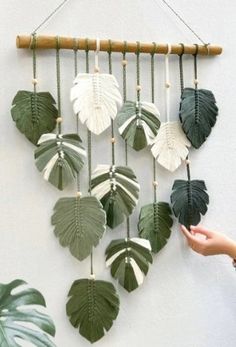 a wall hanging made out of green leaves and white flowers with a hand holding it