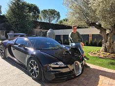 a man sitting on top of a black bugatti parked in front of a tree