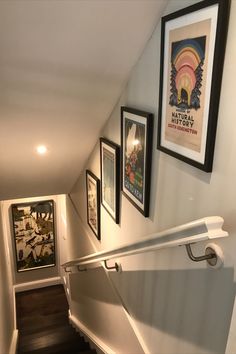 a stairway with pictures on the wall and framed posters above it, along with other art