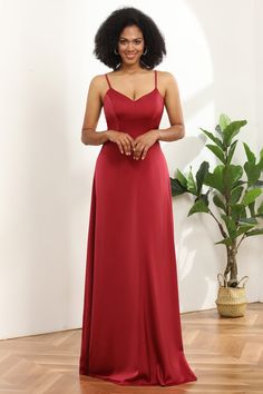 a woman in a long red dress standing on a wooden floor next to a potted plant