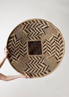 a woman holding up a woven basket with an intricate design on the bottom and sides