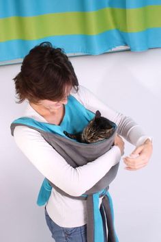 a woman is holding a cat in her sling while wearing a blue and gray vest