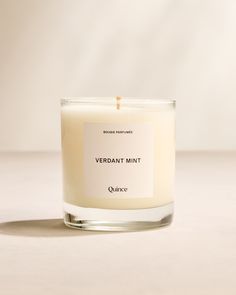 a white candle sitting on top of a table next to a bottle of liquid that says, verdant mint