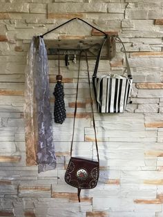 two purses are hanging on the wall next to a scarf and hat rack in a stone walled room